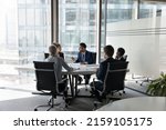 Serious team of professionals, five multi ethnic business people negotiating in modern boardroom, discuss project, consider contract terms and conditions, solve business. Formal meeting event concept