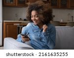 Excited cheerful gen Z African teenager girl using mobile phone, getting surprising good news, looking at screen, laughing, celebrating win, success, luck, achieve, good result