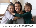 Small photo of Headshot portrait of happy young Caucasian mother hug cuddle with cute small excited children at home. Loving caring two little kids embrace mom show affection and support. Family concept.