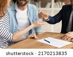 Cropped close up view happy couple receiving keys from new own property, finish meeting in real estate agency lead by realtor in formal suit. Bank mortgage for young family, selling, renting concept