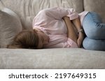 Small photo of Depressed unhappy ill young woman lying on couch in embryo pose, suffering from belly ache, spasm, miscarriage symptoms, feeling strong pain. Health problems, emotional crisis