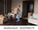 Small photo of Young single man carrying big packed cardboard boxes with personal belongings inside unfurnished living room on relocation to new first own or rented house. Homeowner move day, tenancy, bank mortgage