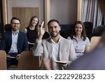 Small photo of Businessman take part in educational, motivational training event seated with colleagues attend together in seminar, raises his arm for ask question, participate in voting, having opinion to share it