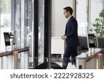 Millennial businessman in formal suit leaving office building area, passes through doorway, security gateway and electronic card reader, working day ended, going at lunch break in modern workplace