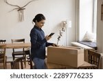 Small photo of Millennial Indian woman sending cardboard box, prepare goods for shipment using smartphone, calling for courier to pick up parcel, use on-line mobile application delivery electronic services. Dispatch