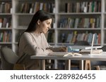 Small photo of Girl prepares for exams in university library, writing exercise, makes notes, jotting information learning theory, sit at desk looks at laptop, reading text, do assignment. New knowledge, modern tech