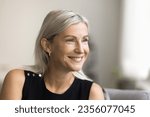 Small photo of Happy mature blonde lady looking away with toothy smile, thinking, dreaming, posing at home, laughing in good thoughts. Positive senior woman close up candid facial portrait