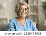 Happy positive blonde elder woman in stylish eyeglasses looking at camera with perfect toothy smile, laughing, posing for home portrait. Beautiful mature lady video call screen head shot