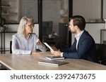 Small photo of Two serious different aged business colleagues discussing project management at meeting table. Younger employee man reporting to senior boss woman. Mature mentor training intern worker