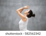 Side view portrait of beautiful young woman wearing sport watch for heart rate and calorie burn control working out against grey wall, doing yoga or pilates exercise. Close up 