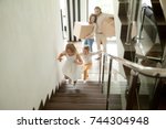 Happy children going upstairs inside two story big house, excited kids having fun stepping walking up stairs running to their rooms while parents holding boxes, family moving in relocating new home 
