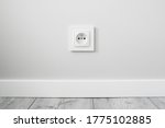 New electrical socket isolated on gray wall. Renovated studio apartment power supply background. Gray wooden floor. Empty copy space white plastic power outlet.