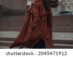 Cropped stylish young woman in fashionable long brown leather coat. Pretty elegant girl model posing. Autumn street style. Casual fashion