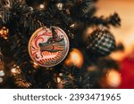 Festive shiny Christmas ball with the image of a dragon hanging on a Christmas tree with golden garland lights. Decorated spruce branches