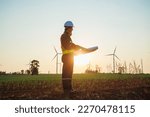 Asian engineer or architect working with his blueprints in hand while supervising construction site in windmills for electricity generation at sunrise background. renewable energy concept.