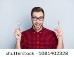 Small photo of Yes! Genial ideas are the most obvious! Close up of thoughtful minded cheerful delighted handsome astonished amazed wondered guy holding light bulb, completed task, isolated on gray background