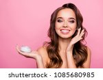 Small photo of Concept of using moisturizing daily cream - beautiful cute pretty charming woman hold a jar of injection and applying it on her cheek bone, isolated on pink background