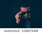 Small photo of Close-up portrait of nice self-content arrogant handsome attractive classy man in blazer touching sunglasses isolated over dark black background