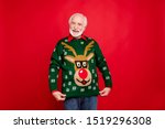 Look I got wonderful present! Portrait of positive cheerful funky old man show his theme christmas party sweater deer decor design wife gift have newyear celebration isolated red color background