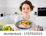 Small photo of Close up photo of pretty housewife lady chef hold ready grilled salmon trout fillet steak with garnish cook dinner one person portion eyes closed wear apron t-shirt modern kitchen indoors