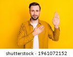 Small photo of Photo of young man hands on chest make oath swear tell truth justice isolated over yellow color background