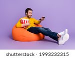 Full length body size photo guy in beanbag laughing watching tv keeping remote controller isolated pastel purple color background