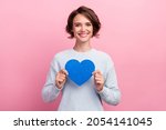 Photo of cheerful nice happy young woman hold hands blue heart paper shape isolated on pink color background