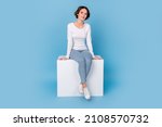 Photo of girlish adorable woman wear white shirt sitting white cube chair isolated blue color background