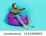 Small photo of Full size profile side photo of young man sit violet beanbag play addicted station isolated over turquoise color background