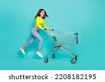 Small photo of Full size profile photo of cool brunette hair young lady run with trolley wear shirt jeans sneakers isolated on teal color background