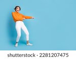Small photo of Full size photo of pretty young girl pulling rope string excited empty space dressed stylish orange look isolated on blue color background