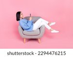 Full size photo of good mood relaxed woman knit pullover trousers look at smartphone sit on arm chair isolated on pink color background