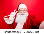 Taking holly jolly x mas festive memories. Funny Saint Nicholas photographer in red traditional outfit, head wear is showing peace gesture and makes shot on camera, isolated on red background