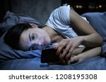 Small photo of Smartphone addiction. Young tired female looking at her mobile phone screen, lying in bed late at night, scrolling her social media news feed