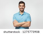 Smiling handsome man in blue polo shirt standing with crossed arms isolated on gray background