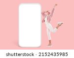 Small photo of Partying girl on pink background in fake fur bomber and stylish shoes feeling light as feather dancing next to vertical gigantic phone template with blank copy space for your promotional content