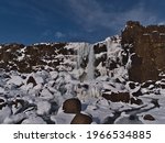 Beautiful front view of Öxarárfoss waterfall in rocky Almannagjá canyon in Þingvellir national park, Golden Circle, Iceland, in winter season with snow and icicles on sunny day.