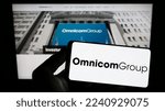 Small photo of Stuttgart, Germany - 12-10-2022: Person holding smartphone with logo of US media company Omnicom Group Inc. on screen in front of website. Focus on phone display. Unmodified photo.