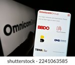 Small photo of Stuttgart, Germany - 12-10-2022: Person holding cellphone with website of US media company Omnicom Group Inc. on screen in front of logo. Focus on center of phone display. Unmodified photo.