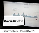 Small photo of Stuttgart, Germany - 12-10-2022: Person holding mobile phone with logo of American media company Omnicom Group Inc. on screen in front of web page. Focus on phone display. Unmodified photo.