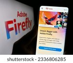 Small photo of Stuttgart, Germany - 07-15-2023: Person holding cellphone with webpage of generative AI product Adobe Firefly on screen in front of logo. Focus on center of phone display. Unmodified photo.