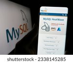 Small photo of Stuttgart, Germany - 07-13-2023: Person holding cellphone with website of relational database management system MySQL on screen in front of logo. Focus on center of phone display. Unmodified photo.