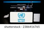 Small photo of Stuttgart, Germany - 11-03-2023: Person holding mobile phone with logo of United Nations Plalestine refugees agency UNRWA in front of web page. Focus on phone display. Unmodified photo.