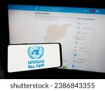 Small photo of Stuttgart, Germany - 11-03-2023: Person holding cellphone with logo of United Nations Plalestine refugees agency UNRWA in front of webpage. Focus on phone display. Unmodified photo.