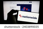 Small photo of Stuttgart, Germany - 12-14-2023: Person holding mobile phone with logo of British financial institution Nationwide Building Society in front of web page. Focus on phone display. Unmodified photo.