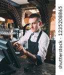 Small photo of small business, people and service concept - happy man or waiter in apron at counter with cashbox working at bar or coffee shop