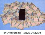 A smart phone placed on multiple naira notes, cash or nigerian currency spread on a blue surface