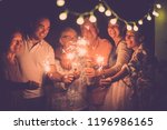 group of caucasian people friends with different ages celebrate together a birthday or new year eve by night outdoor at home. lights and sparkles  with cheerful women and men having fun in friendship