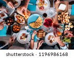 Above aerial view of group of friends having fun eating together at lunch or dinner with a table full of different and colorful food and technology mobile phone. mix of hands of caucasian people 
