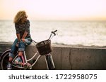 Small photo of People enjoying outdoor leisure actvity looking a beautiful coloured sunset - beautiful adult young woman with long curly blonde hair enjoy the relax after a bike tour - horizon and sun with ocean